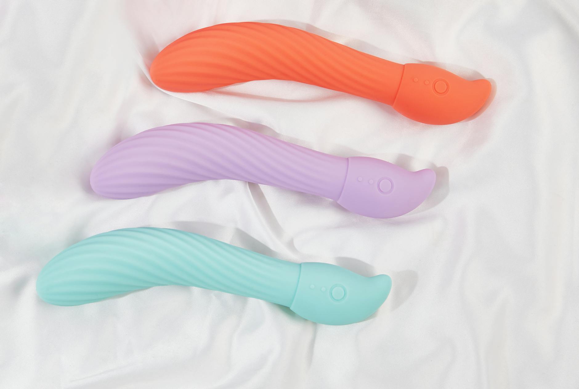 Three colorful clitoral vibrators arranged on white fabric, highlighting smooth texture and design