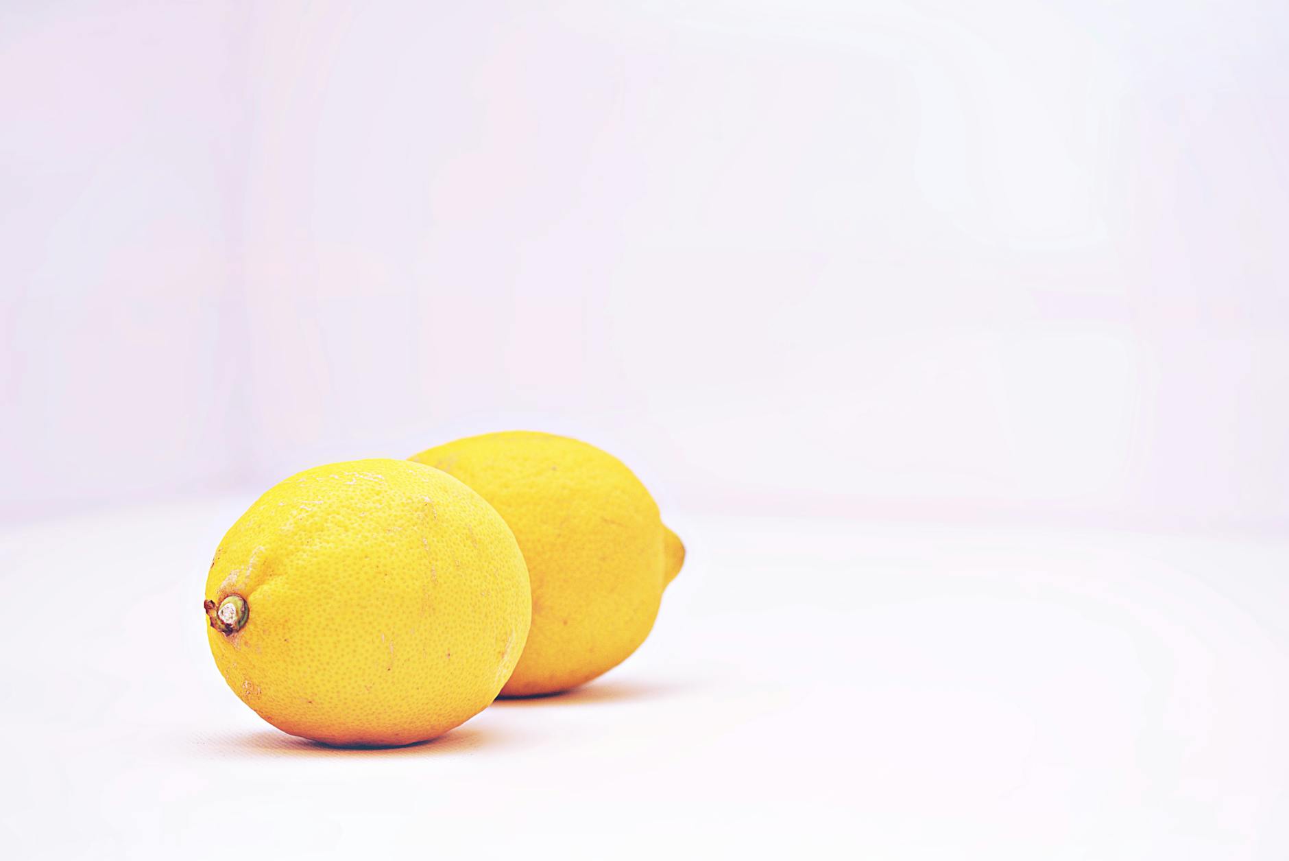 Two vibrant lemons against a minimalistic white background, representing fresh and simple pleasure.