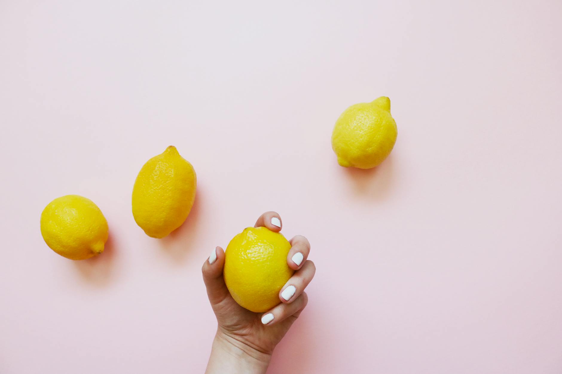 A hand holding a lemon on a soft pink background