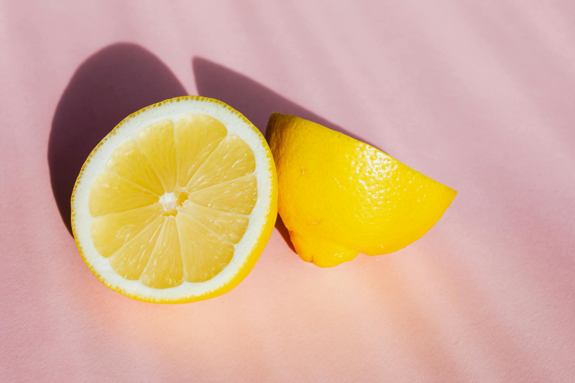 Fresh lemon halves on a pink background in sunlight, symbolizing clarity and sensation