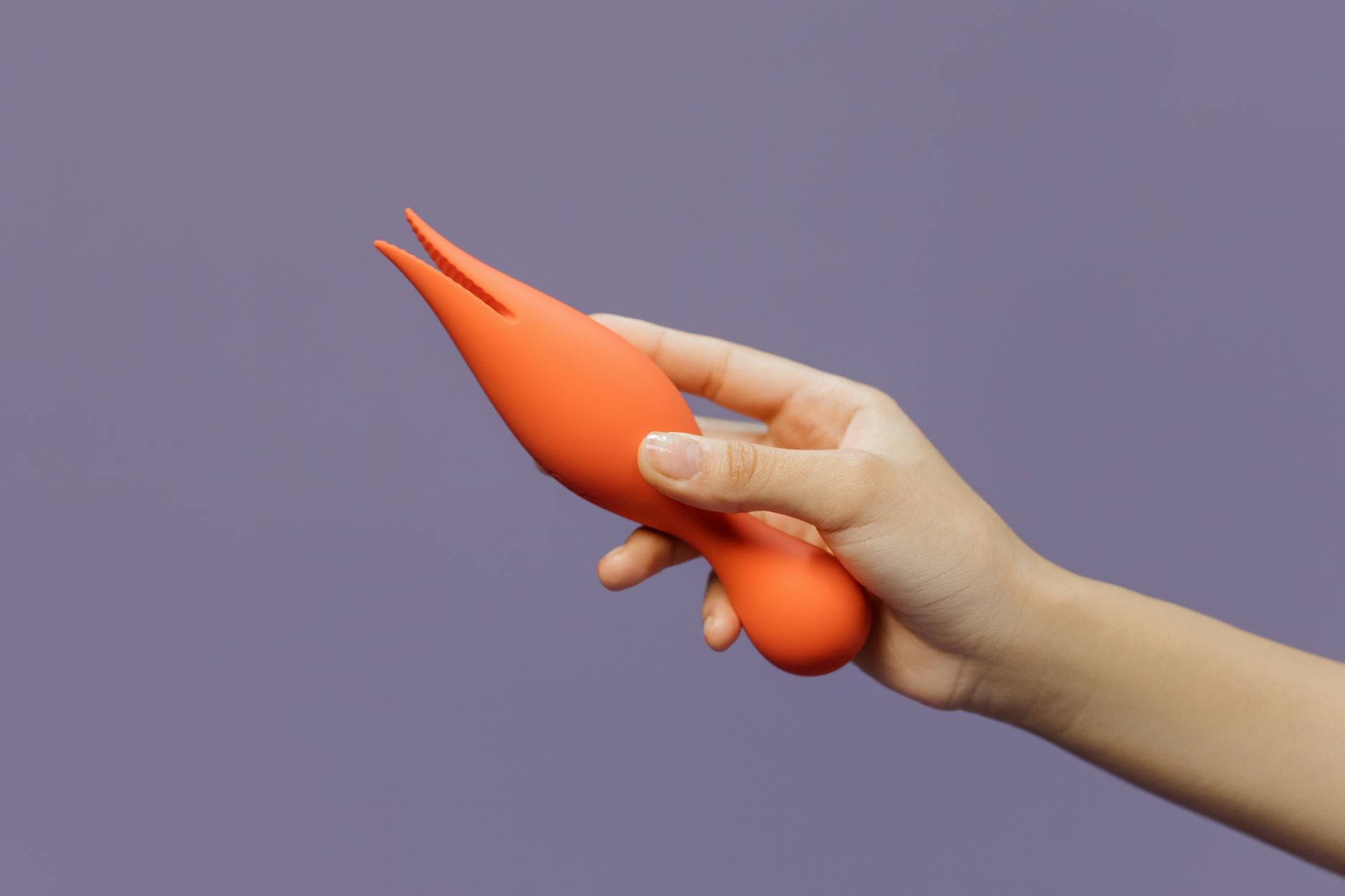 A close-up of a hand holding a lemon vibrator against a minimalistic purple backdrop
