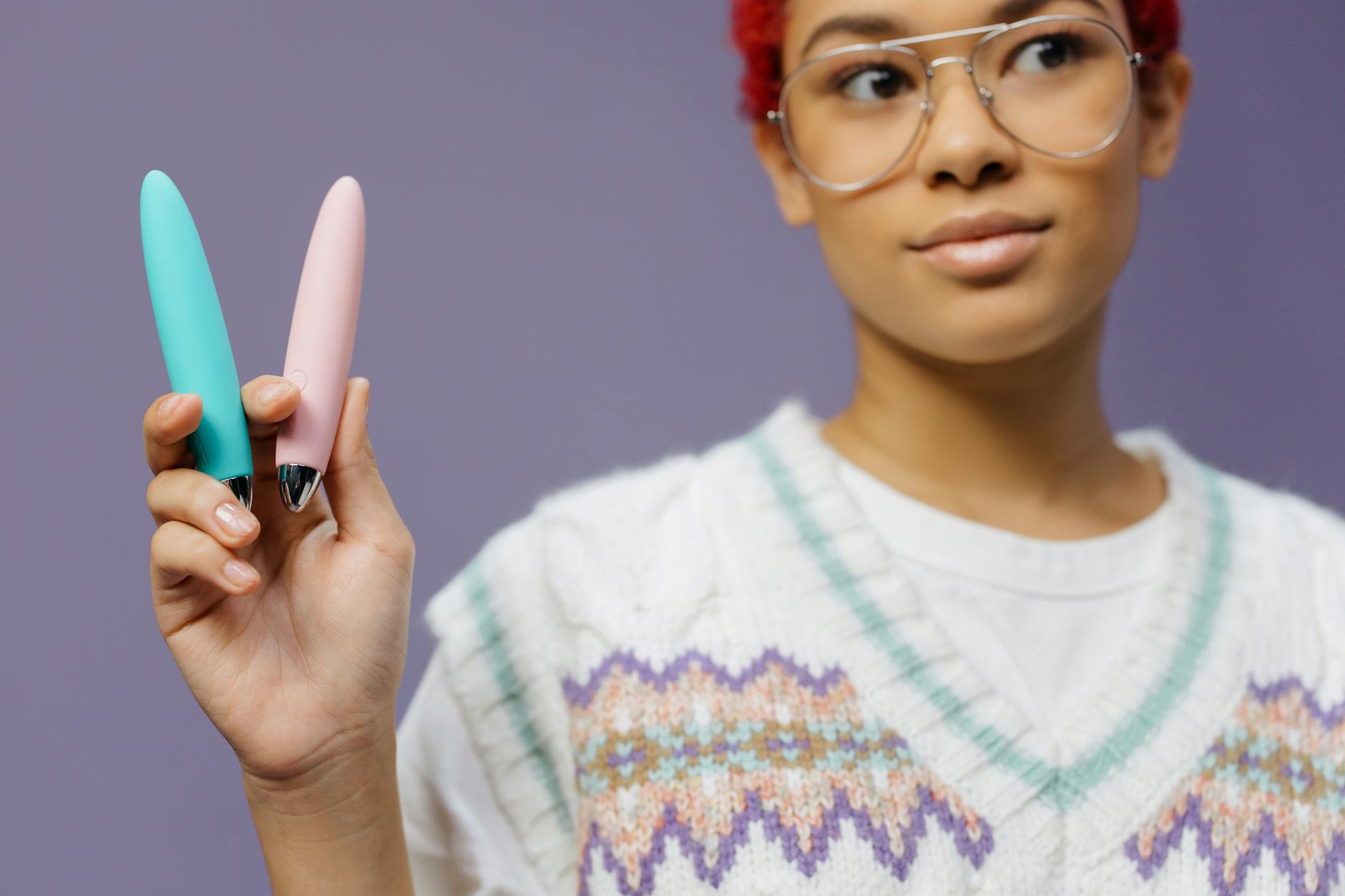 Woman holding two vibrators against purple background, symbolizing choice and self-pleasure