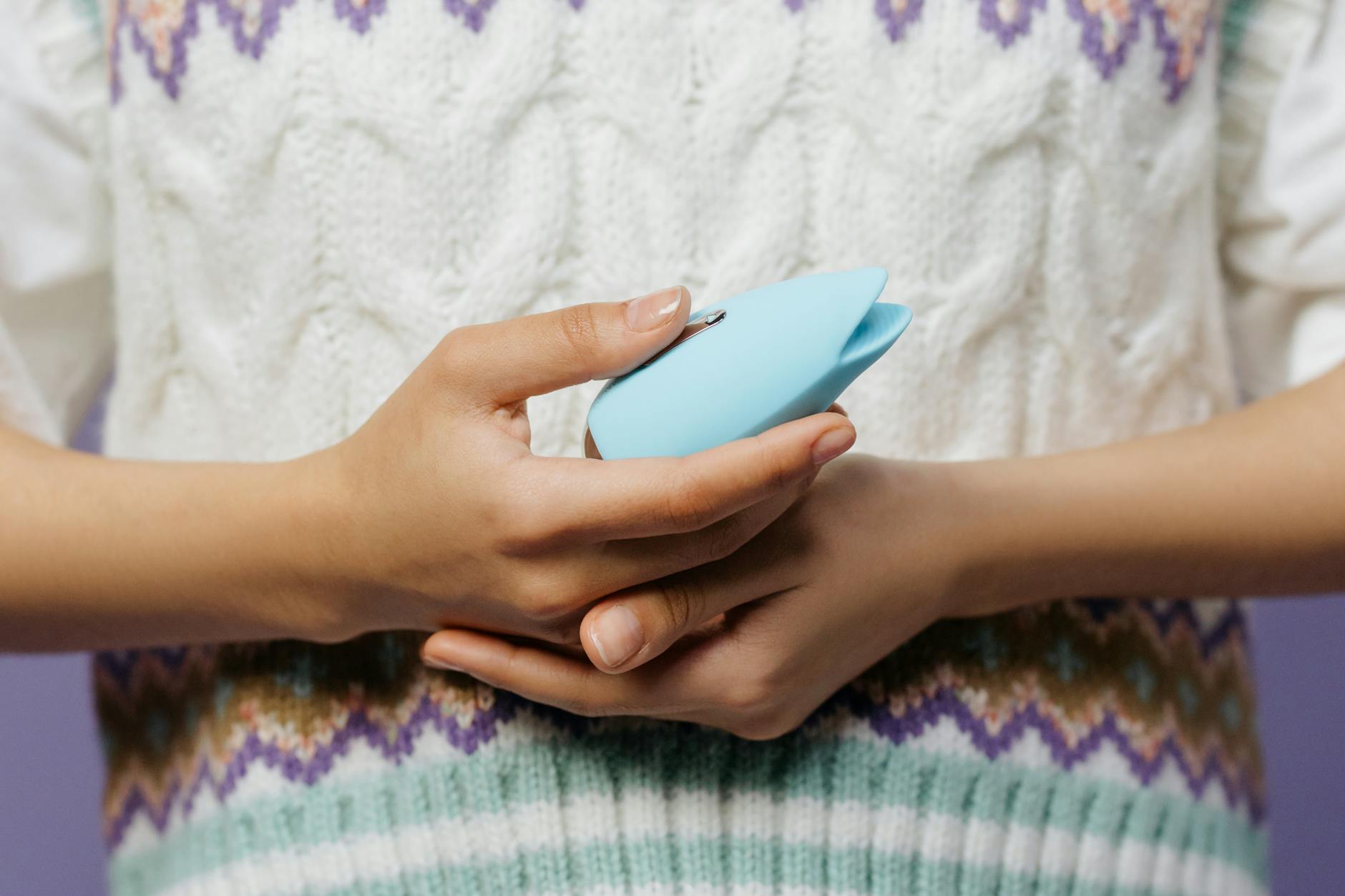A blue silicone clitoral vibrator held in hand against a purple background