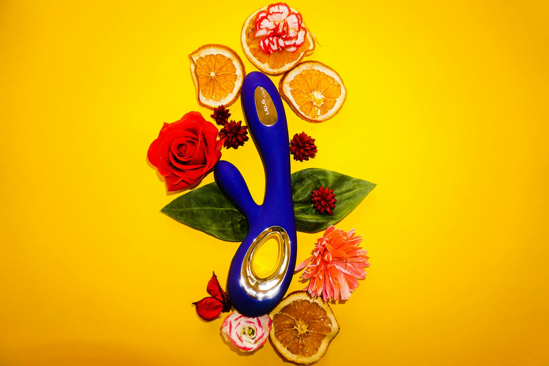 A vibrant lemon clitoral vibrator surrounded by fresh lemons and botanical elements on a bright yellow background